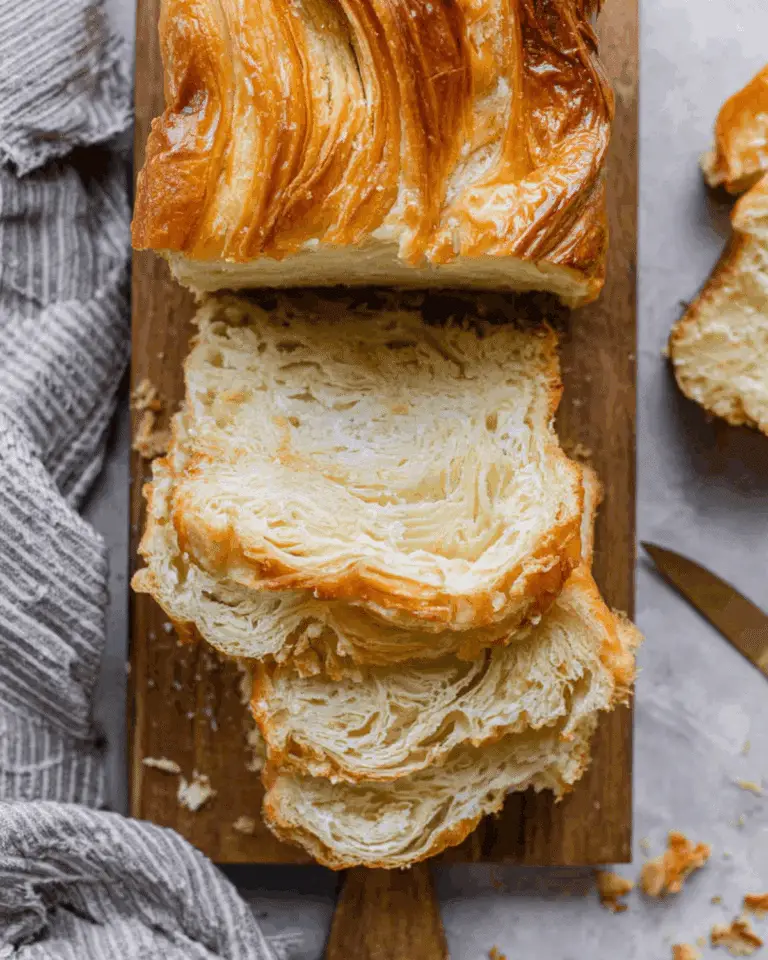 Sliced Croissant Bread Loaf with golden, flaky layers on a wooden cutting board.
