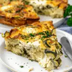 A slice of crustless zucchini quiche on a white plate, showing creamy layers of egg, cheese, and zucchini, garnished with chopped parsley.