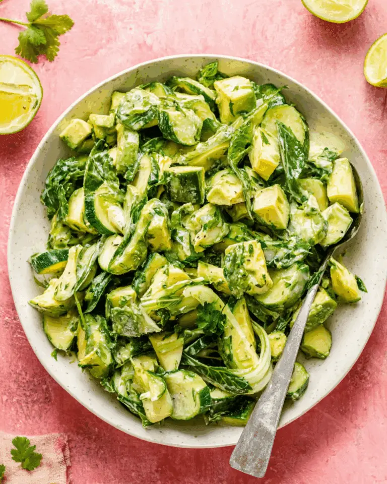 Bowl of cucumber avocado salad with creamy dressing, herbs, and lime on a pink background.