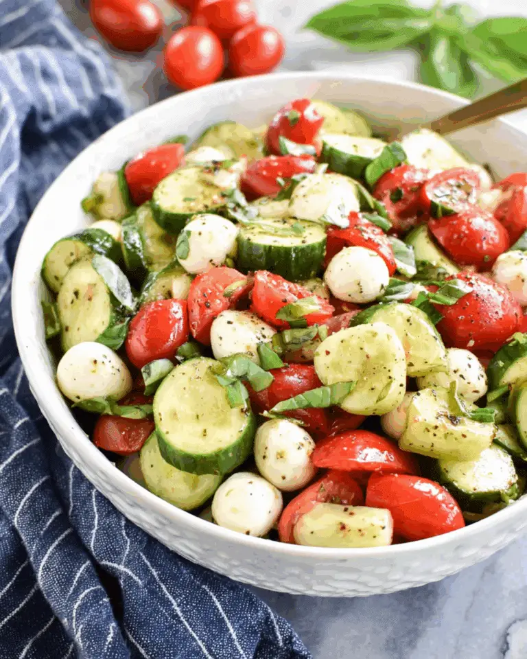 A white bowl filled with Easy Cucumber Caprese Salad made with cherry tomatoes, cucumber slices, mozzarella balls, fresh basil, and black pepper.