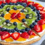 Easy fruit and cracker pizza topped with sliced strawberries, kiwi, blueberries, oranges, and cream on a cookie crust.