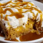 A slice of easy pumpkin spice poke cake topped with whipped cream and caramel sauce on a white plate.