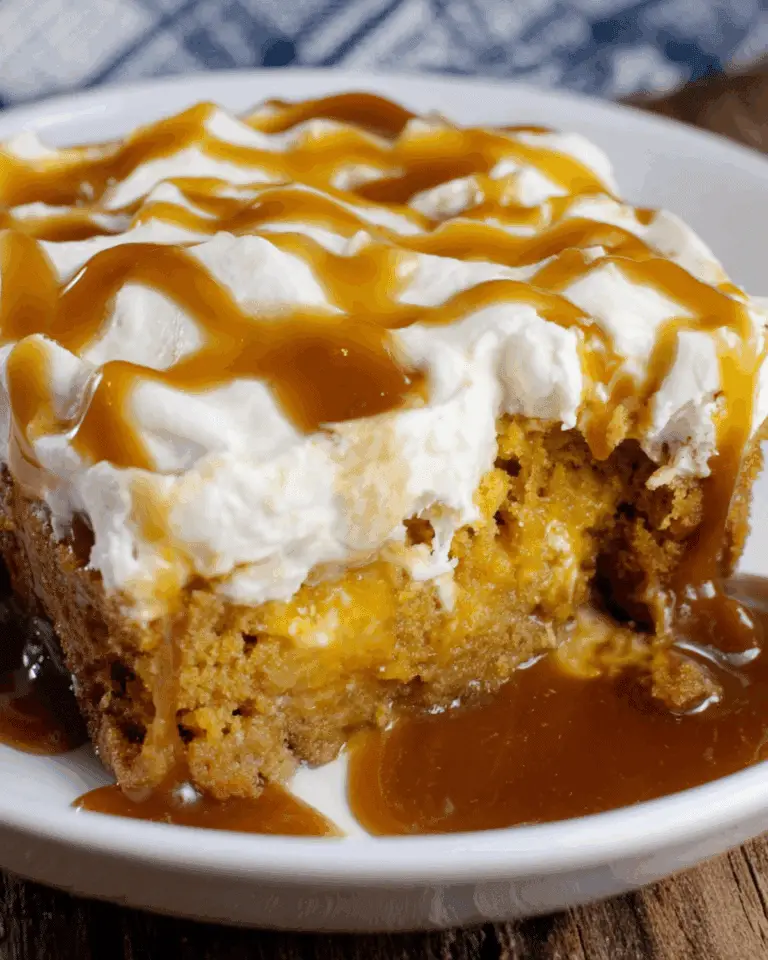 A slice of easy pumpkin spice poke cake topped with whipped cream and caramel sauce on a white plate.