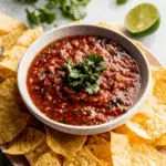 Bowl of fire roasted salsa topped with fresh cilantro, surrounded by crispy tortilla chips.