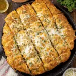 Skillet of golden Focaccia Cheesy Garlic Bread topped with melted cheese and herbs.