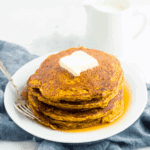 Stack of healthy low carb pumpkin pancakes topped with butter and maple syrup on a white plate.