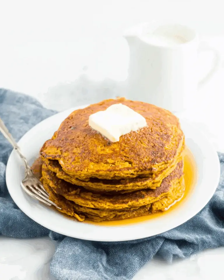 Stack of healthy low carb pumpkin pancakes topped with butter and maple syrup on a white plate.