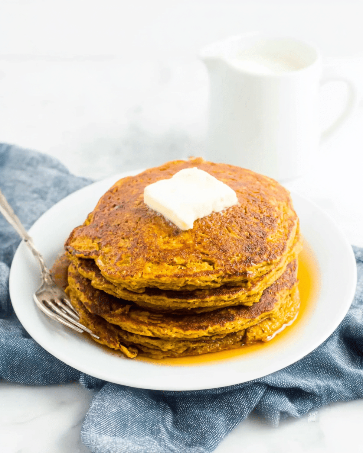 Stack of healthy low carb pumpkin pancakes topped with butter and maple syrup on a white plate.