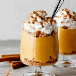 Healthy pumpkin mousse in a glass topped with whipped cream and crushed graham crackers, served with a spoon.