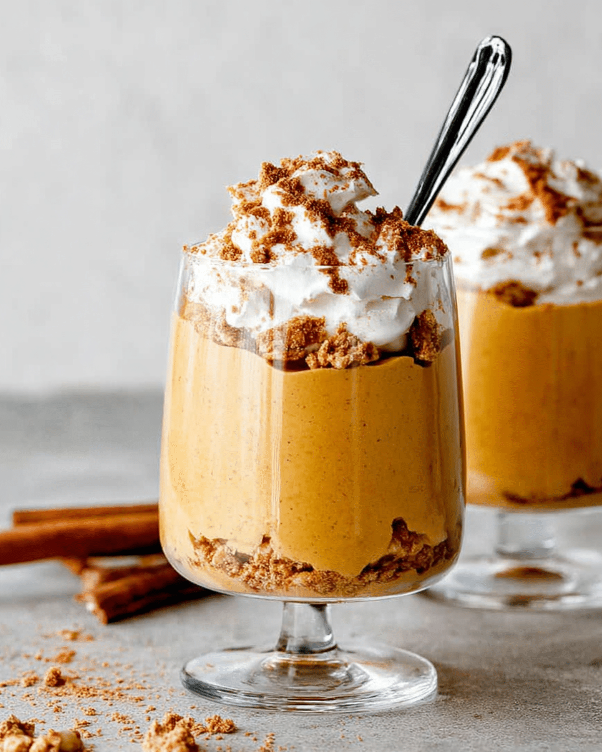 Healthy pumpkin mousse in a glass topped with whipped cream and crushed graham crackers, served with a spoon.