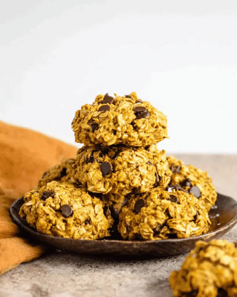 Healthy pumpkin oat cookies with chocolate chips stacked on a dark plate, with an orange napkin in the background.