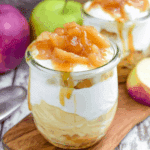 No Bake Caramel Apple Pie Cheesecake Parfaits in glass jars, layered with apple filling, cheesecake mousse, and caramel sauce.