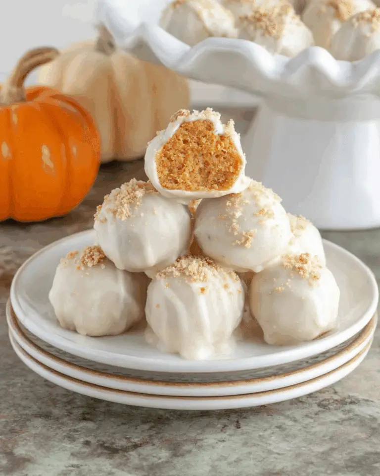 No-Bake Pumpkin Pie Bites stacked on a white plate, coated in white chocolate and topped with graham cracker crumbs.
