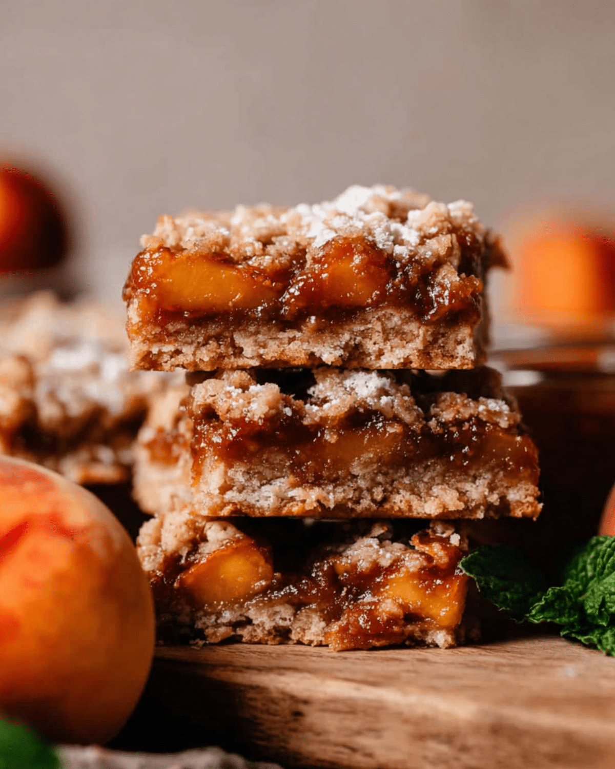 A close-up of stacked Peach Bars with a golden crumble topping and gooey peach filling, dusted lightly with powdered sugar.