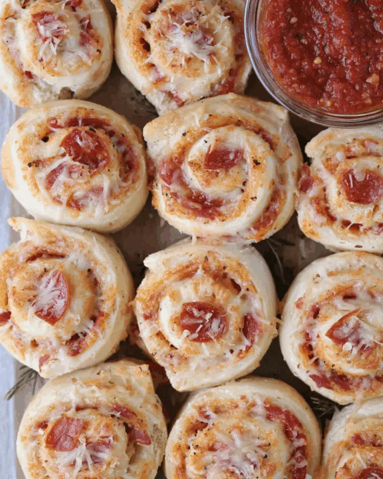 A batch of freshly baked Pepperoni Pizza Rolls topped with melted cheese, served with a bowl of marinara dipping sauce.