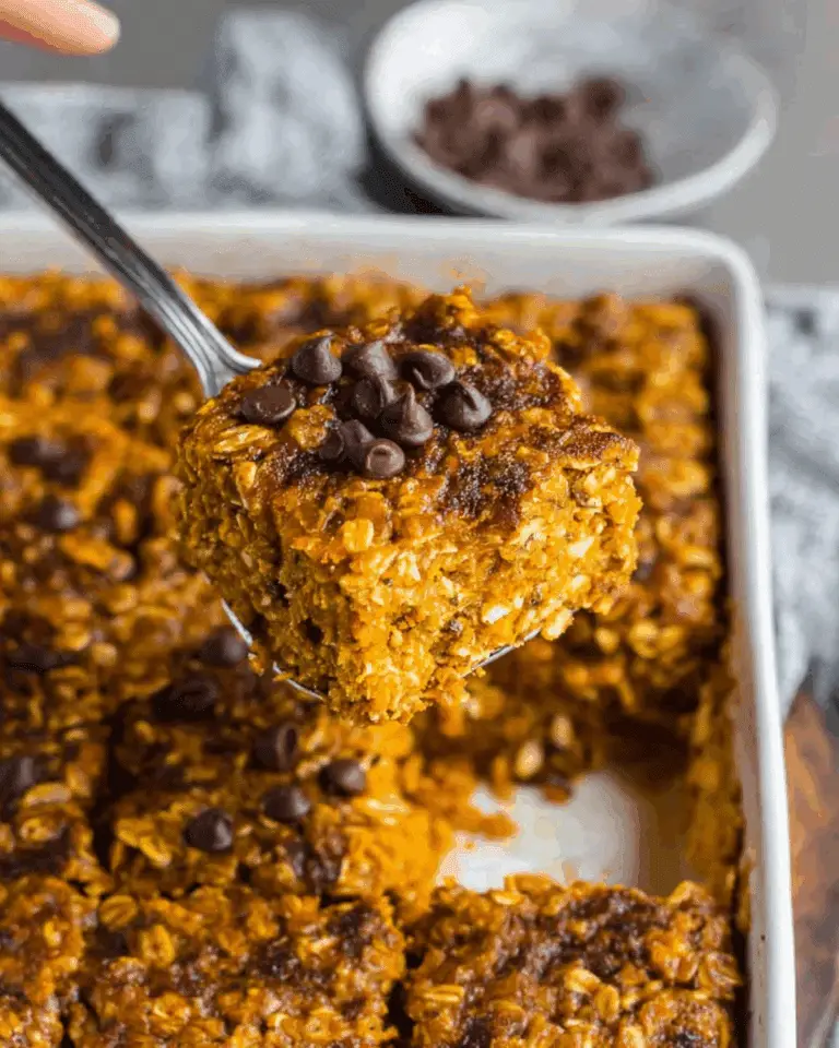 A square of pumpkin baked oatmeal topped with chocolate chips being lifted from a baking dish.