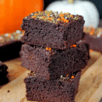 Stack of rich, moist pumpkin brownies topped with festive orange and green sprinkles on a wooden board.