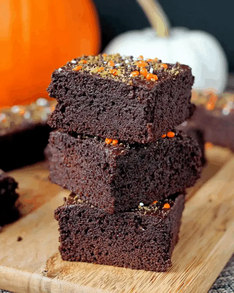 Stack of rich, moist pumpkin brownies topped with festive orange and green sprinkles on a wooden board.