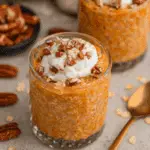 Glass of pumpkin pie overnight oats topped with whipped cream and chopped pecans.