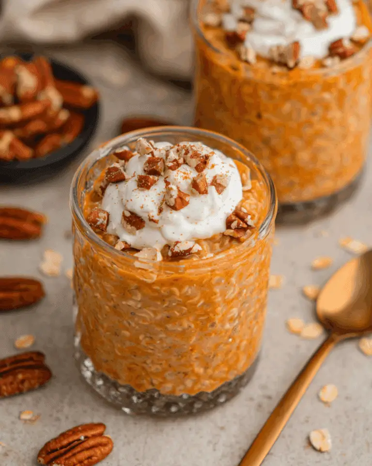 Glass of pumpkin pie overnight oats topped with whipped cream and chopped pecans.