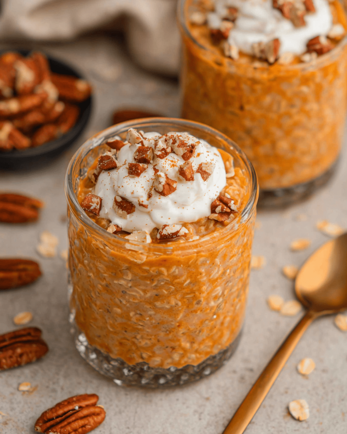 Glass of pumpkin pie overnight oats topped with whipped cream and chopped pecans.