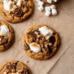 Pumpkin S'mores Cookies topped with toasted marshmallows, melted chocolate, and graham cracker chunks on parchment paper.