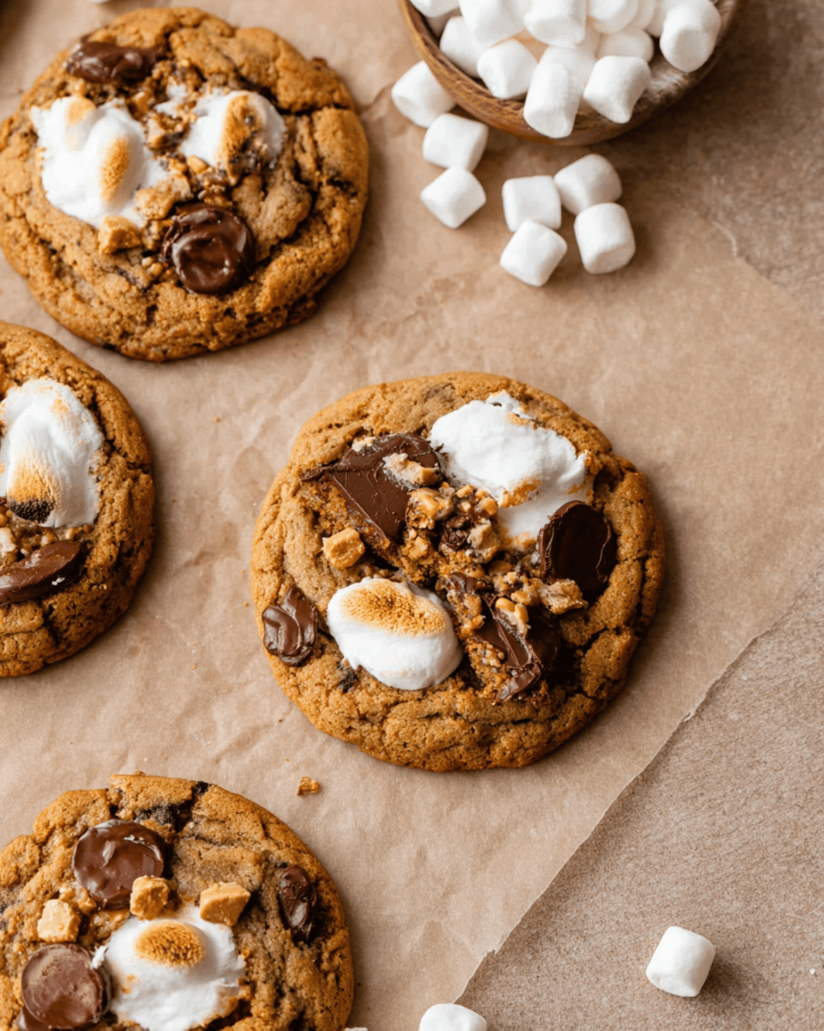 Pumpkin S'mores Cookies topped with toasted marshmallows, melted chocolate, and graham cracker chunks on parchment paper.
