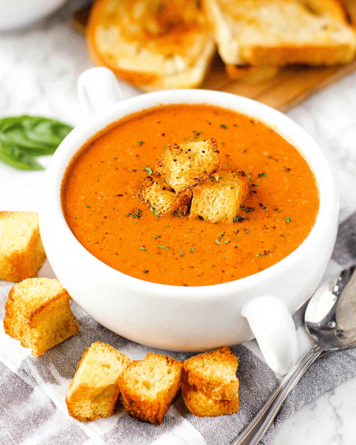 A bowl of roasted tomato basil soup topped with croutons, served with toasted bread.