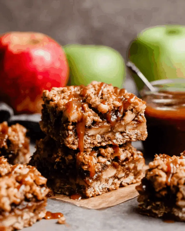 Salted caramel apple bars stacked with gooey caramel drizzle, surrounded by fresh red and green apples.