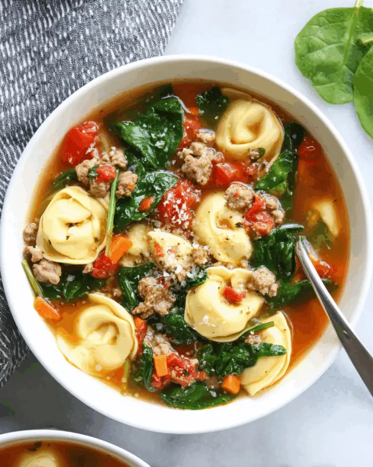 Sausage Tortellini Soup with Spinach in a white bowl, filled with cheese tortellini, sausage, tomatoes, carrots, and fresh spinach.