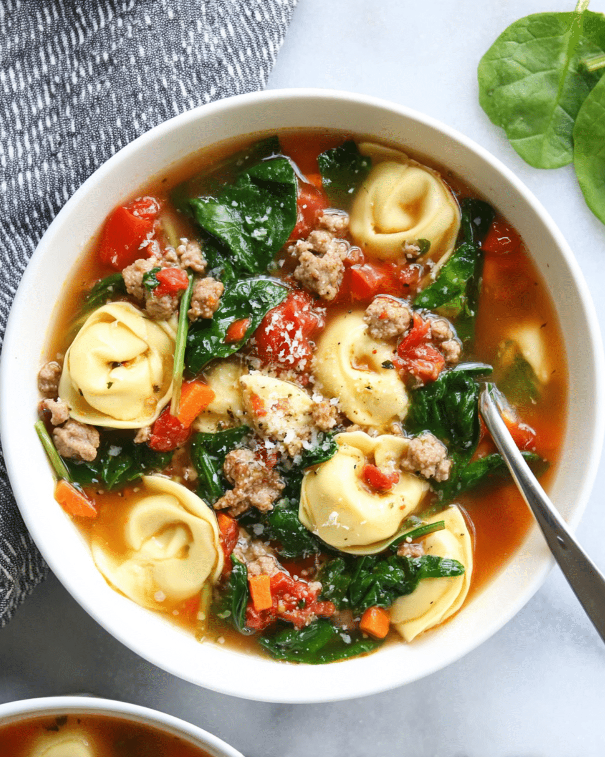 Sausage Tortellini Soup with Spinach in a white bowl, filled with cheese tortellini, sausage, tomatoes, carrots, and fresh spinach.
