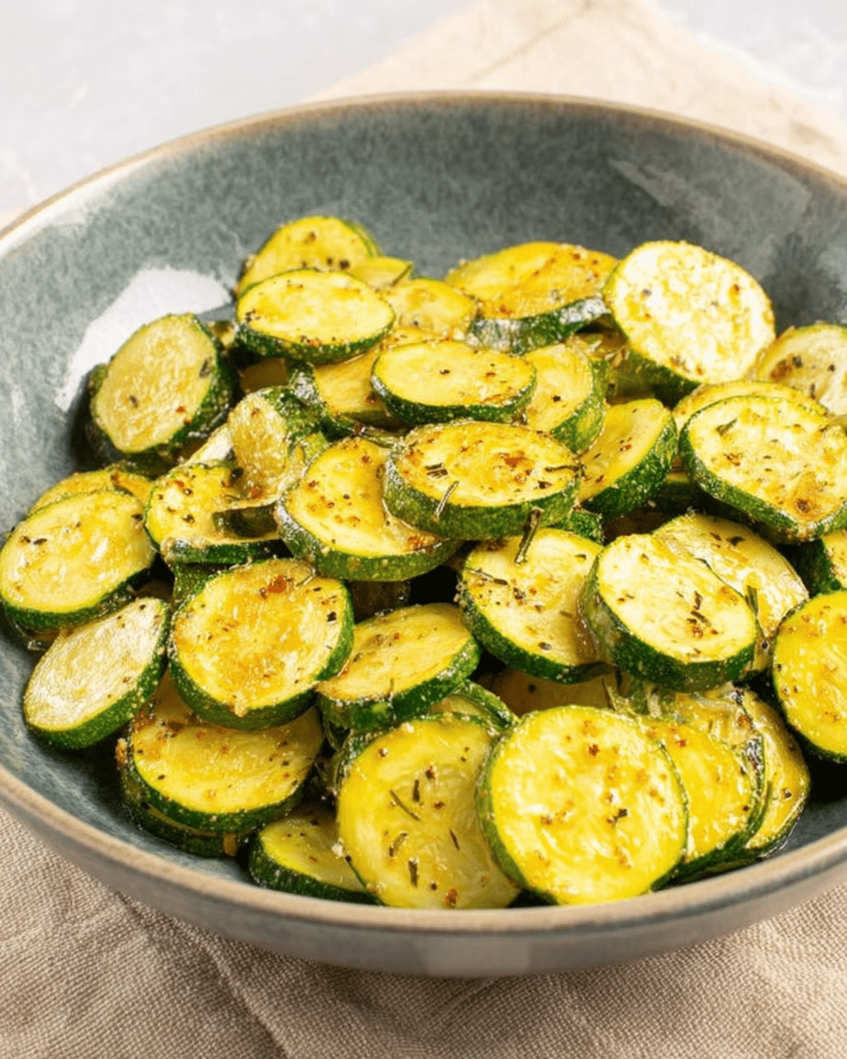 A bowl of sautéed zucchini slices seasoned with herbs and spices, glistening with olive oil.