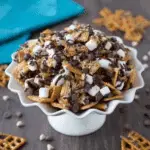 S'mores Snack Mix with cereal, marshmallows, pretzels, and chocolate chips drizzled with melted chocolate in a white serving dish.