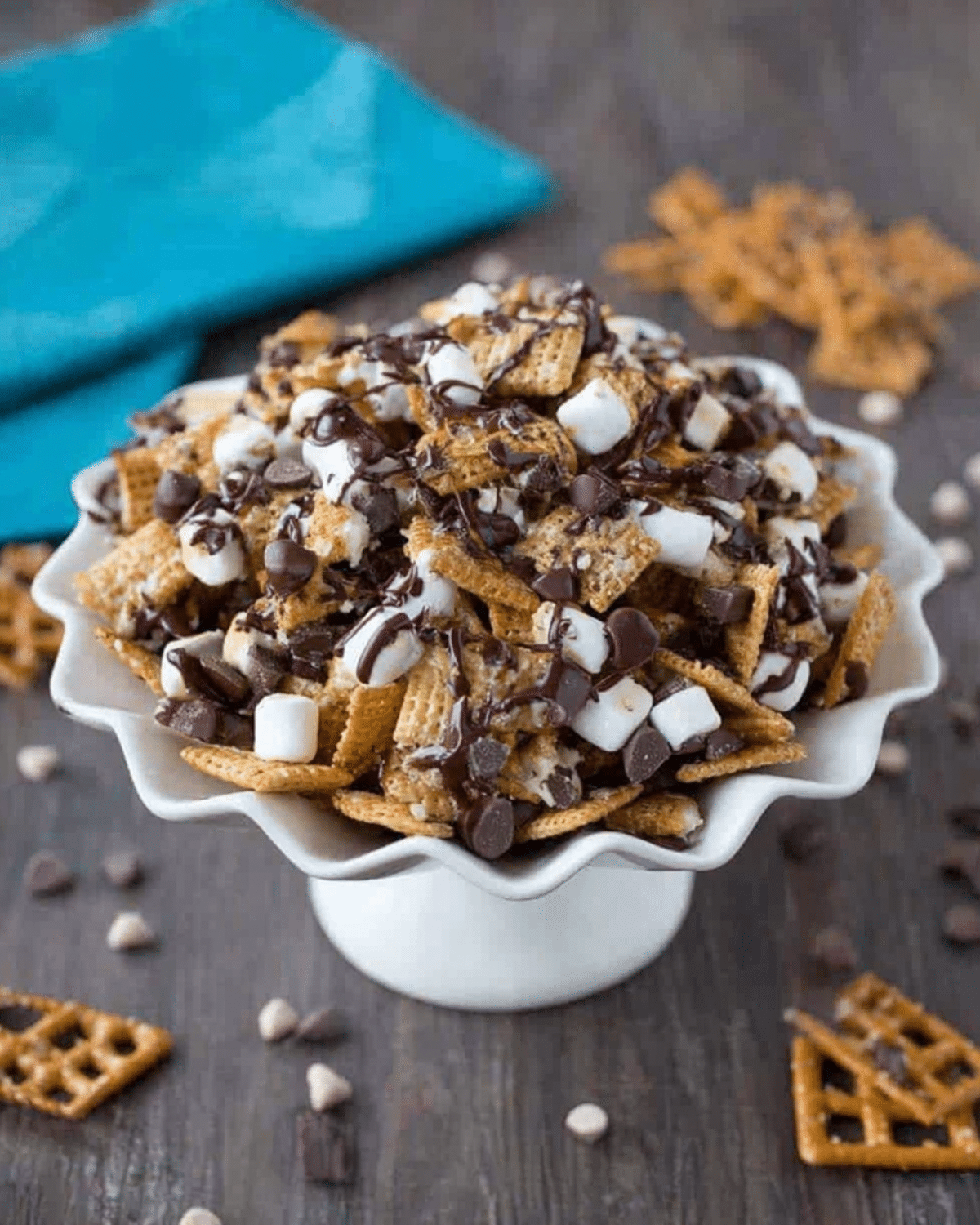 S'mores Snack Mix with cereal, marshmallows, pretzels, and chocolate chips drizzled with melted chocolate in a white serving dish.