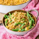 A bowl of Southern green bean casserole topped with golden crispy stuffing, placed on a red patterned cloth.