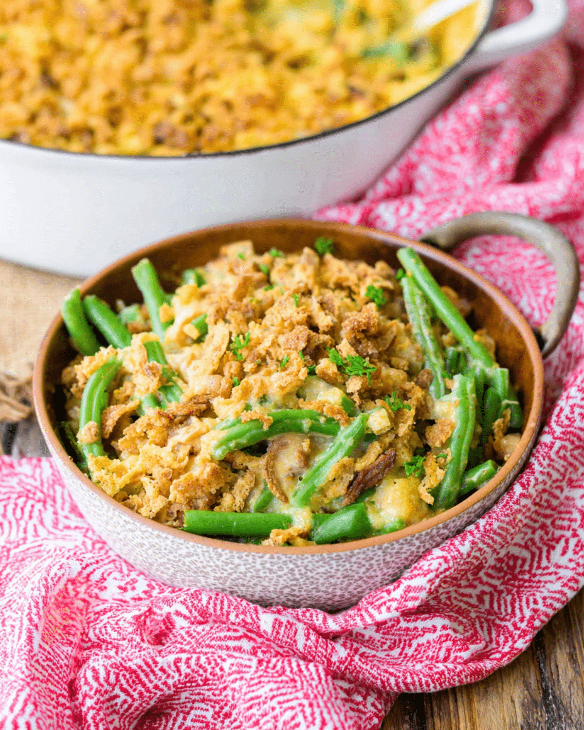 A bowl of Southern green bean casserole topped with golden crispy stuffing, placed on a red patterned cloth.