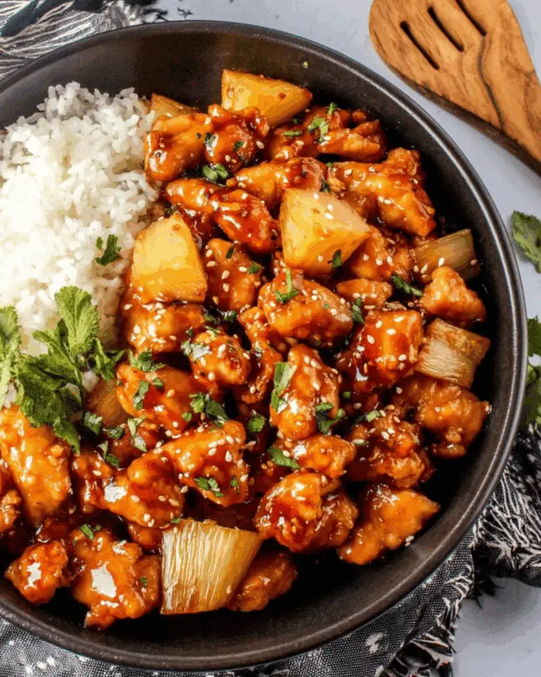 A black bowl filled with Sticky Pineapple Chicken, garnished with sesame seeds and cilantro, served alongside steamed white rice.