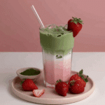 Strawberry Matcha Latte in a clear glass with pink strawberry milk and green matcha layers, topped with ice and fresh strawberry garnish.