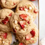 Soft and chewy strawberry shortcake cookies topped with fresh strawberry chunks and white chocolate chips, arranged on a tray.