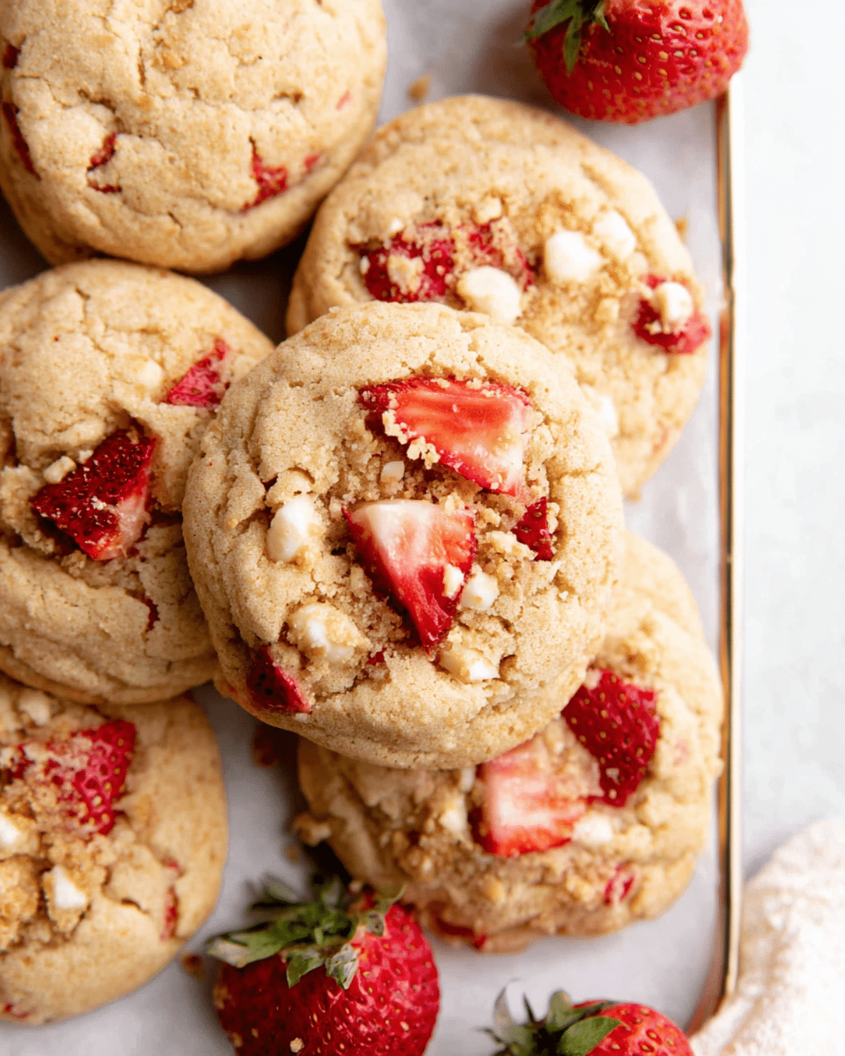 Soft and chewy strawberry shortcake cookies topped with fresh strawberry chunks and white chocolate chips, arranged on a tray.