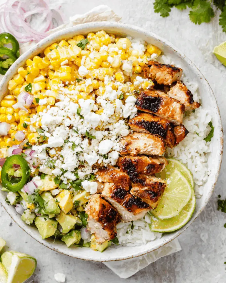Street corn chicken rice bowl topped with grilled chicken, corn, avocado salsa, white rice, feta cheese, and lime slices.