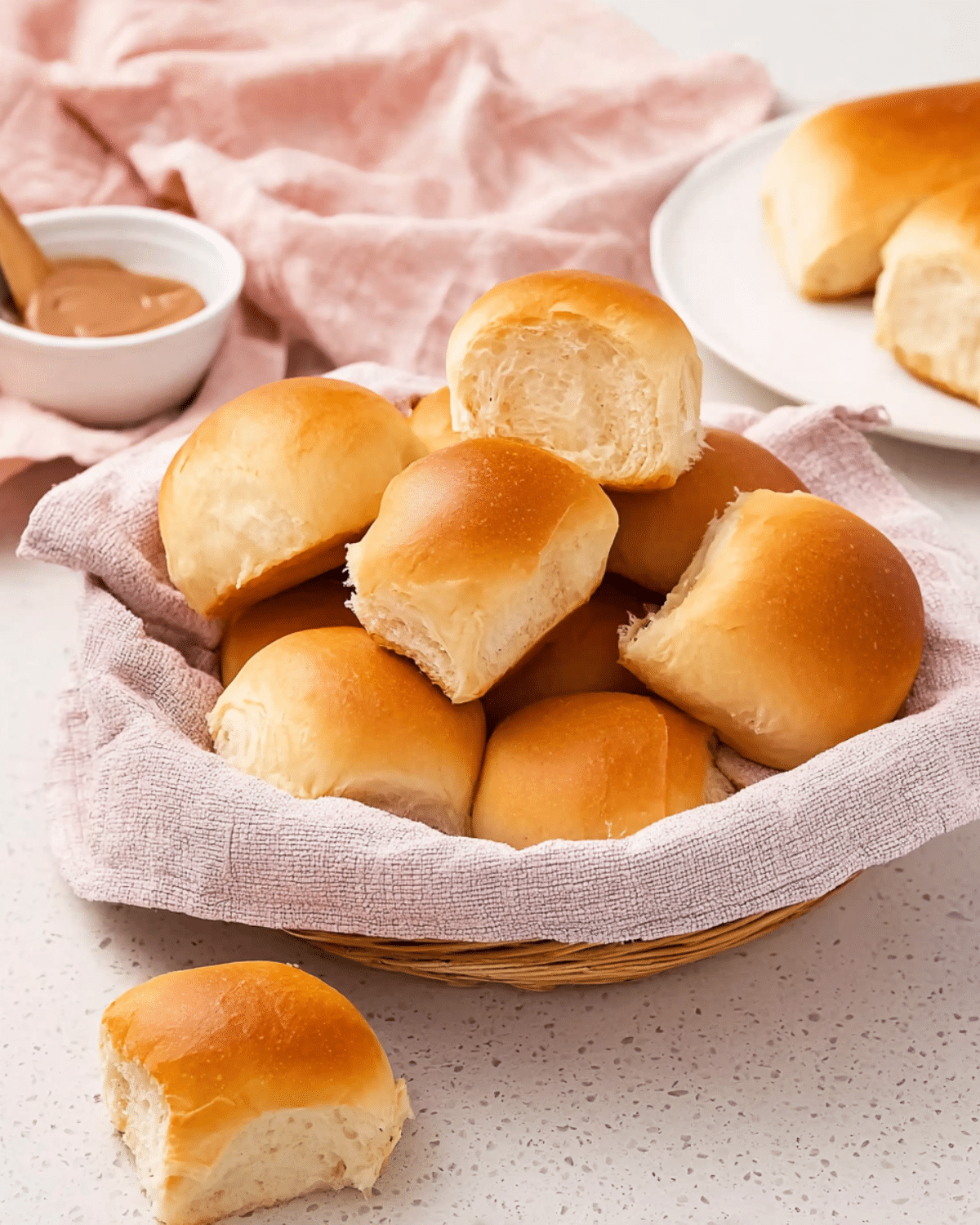 Freshly baked Texas Roadhouse rolls in a basket lined with a pink cloth, with a bowl of cinnamon butter in the background.