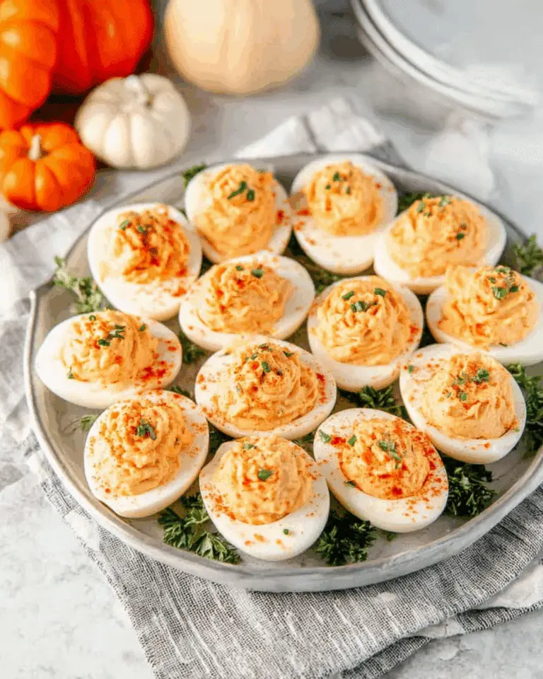 A platter of Thanksgiving appetizer deviled eggs garnished with paprika and chopped herbs, surrounded by small pumpkins and festive decor.