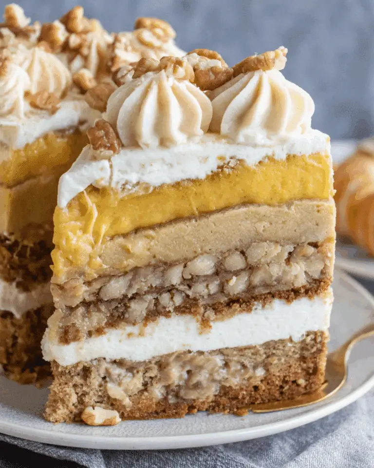 Thanksgiving Piecaken slice featuring layers of pumpkin pie, pecan pie, spice cake, cheesecake, and whipped frosting, topped with piped cream and chopped pecans.