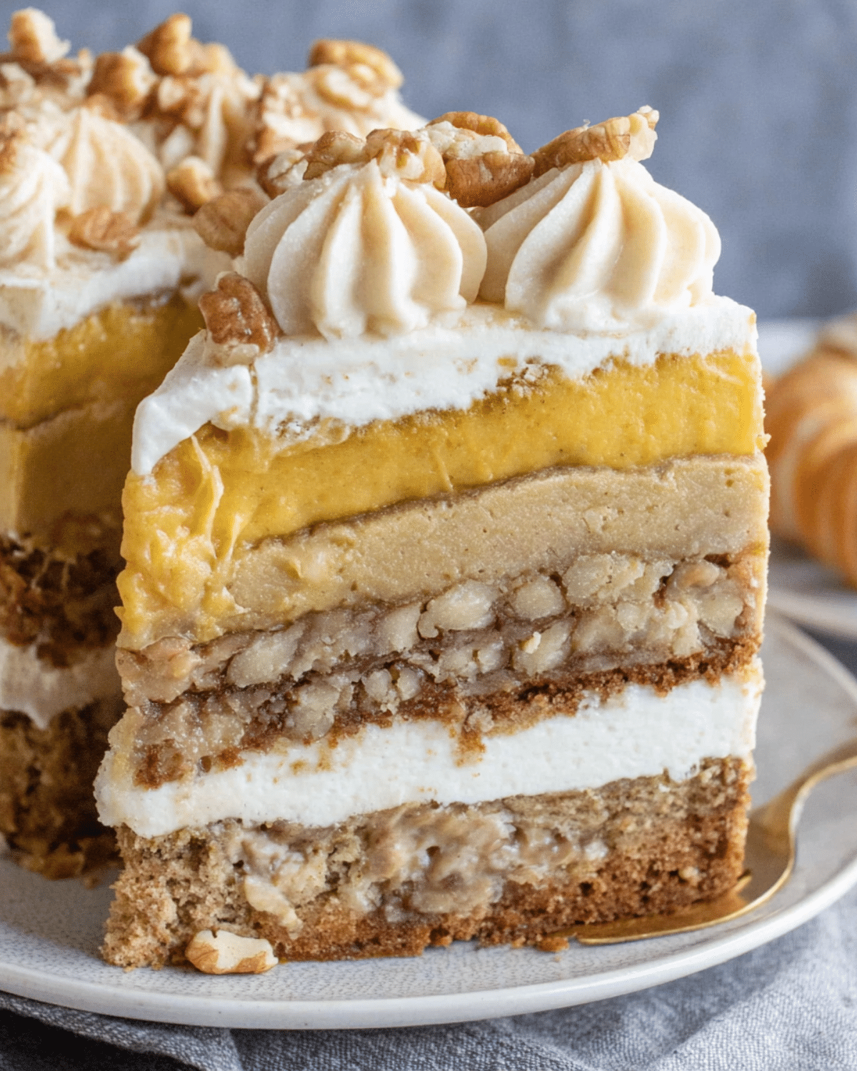 Thanksgiving Piecaken slice featuring layers of pumpkin pie, pecan pie, spice cake, cheesecake, and whipped frosting, topped with piped cream and chopped pecans.