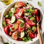 Bowl of tomato, cucumber and onion salad with fresh basil and a drizzle of olive oil.