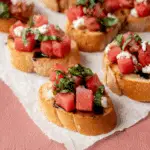 Watermelon bruschetta topped with fresh basil, feta cheese, and balsamic glaze on toasted baguette slices.