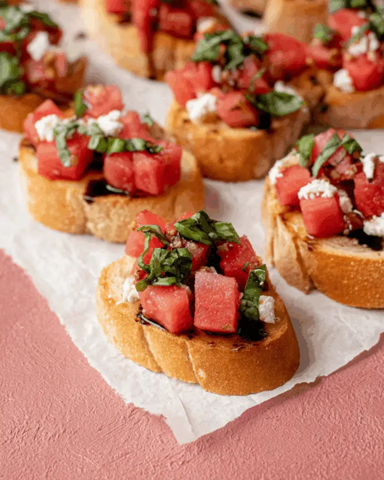 Watermelon bruschetta topped with fresh basil, feta cheese, and balsamic glaze on toasted baguette slices.