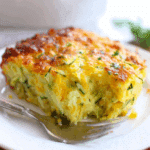 A slice of zucchini cornbread casserole on a white plate, showing its golden crust and moist interior filled with shredded zucchini and cornmeal.