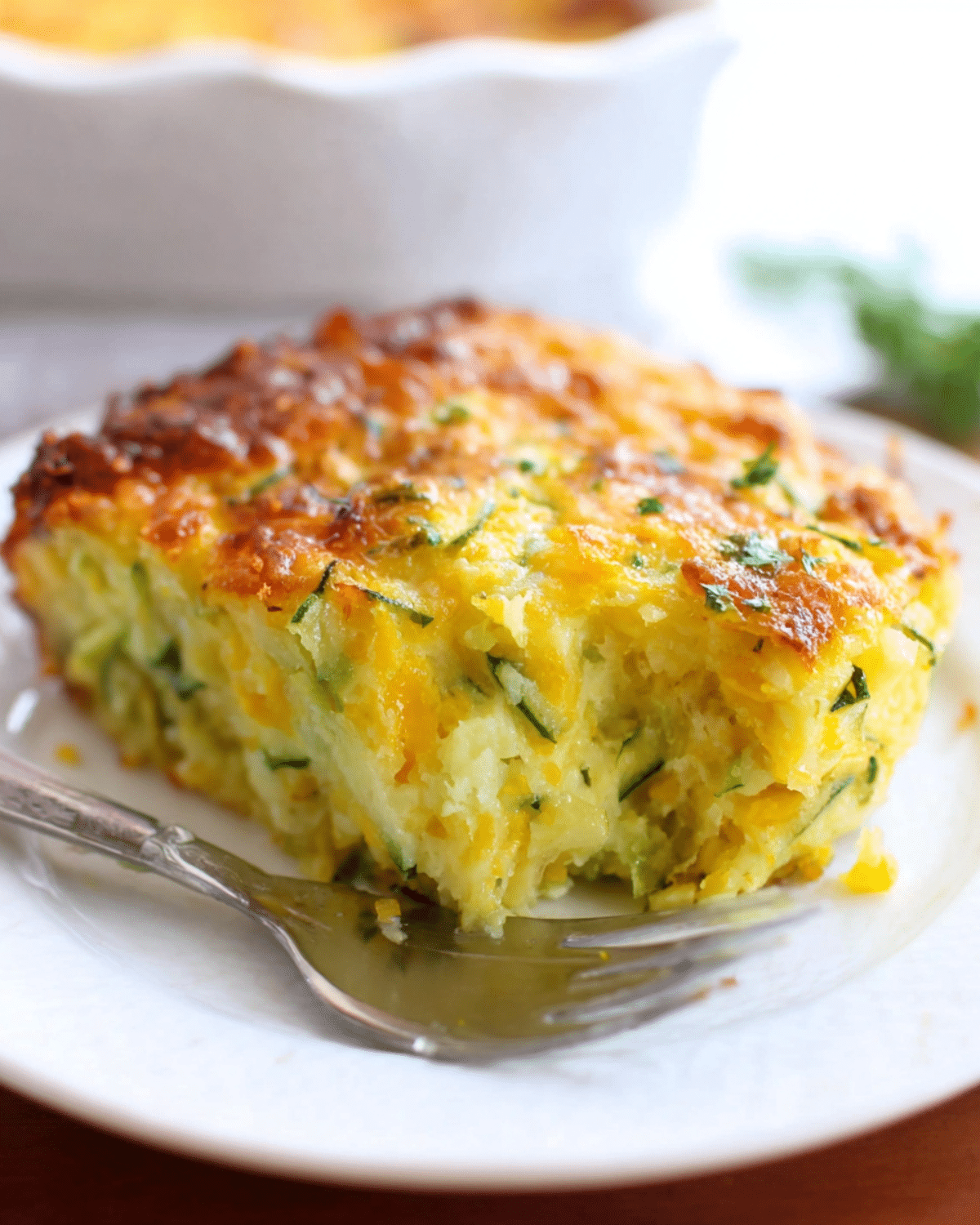 A slice of zucchini cornbread casserole on a white plate, showing its golden crust and moist interior filled with shredded zucchini and cornmeal.